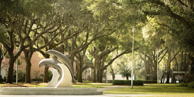 Photo of the JU dolphin statues in the middle of campus with the oak tree walk in the background