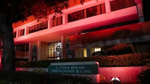 A view of the Howard Building on campus, lit up pink.
