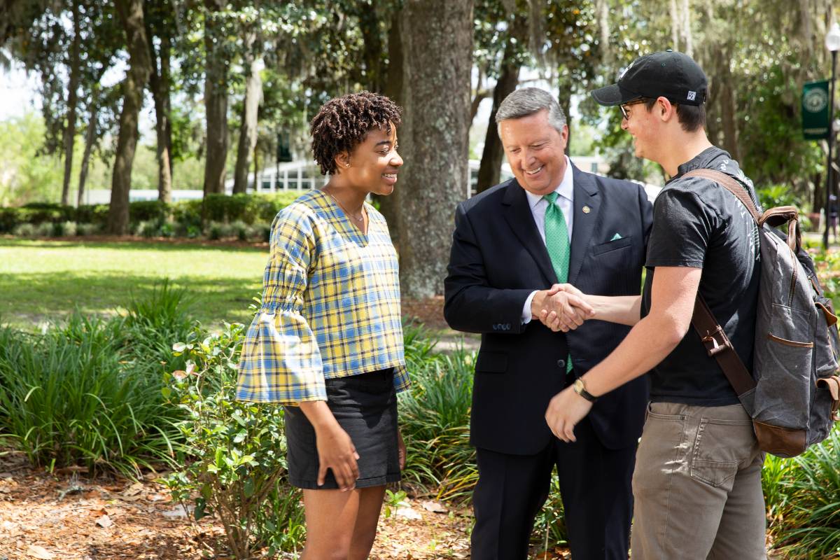 Two students talking with JU President Tim Cost in courtyard on campus