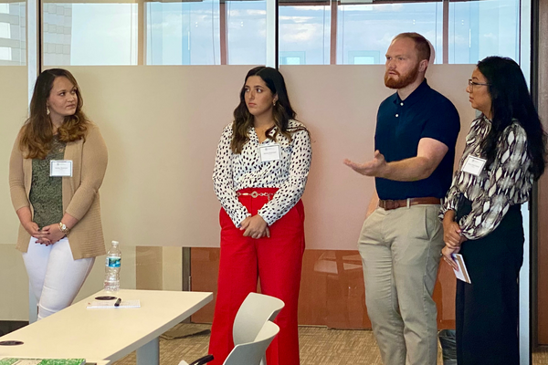 A group of students, three female and one male, standing in a classroom and having a conversation.