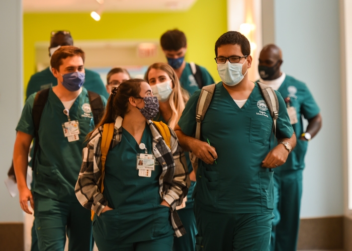 Group of male and female nurses walk through hallway together chatting