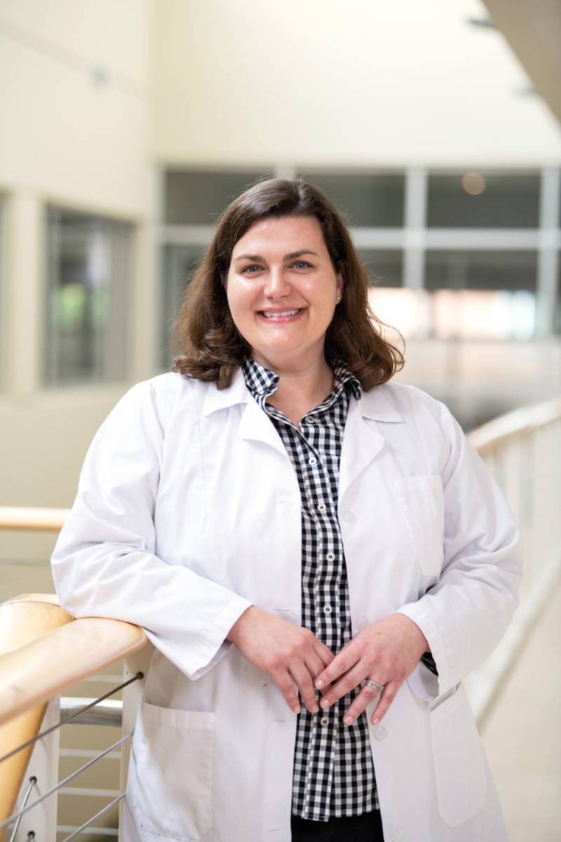 A nurse smiling at the camera in her white coat.