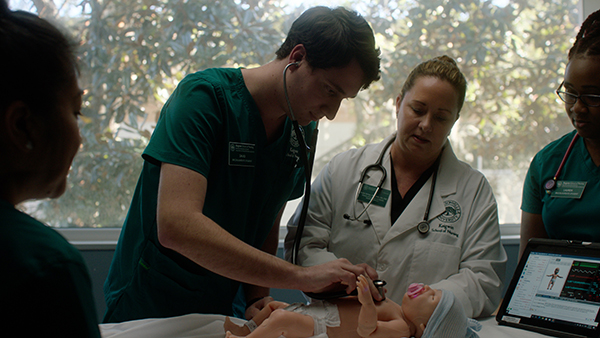 A student performs a simulation on a medical manikin with the aid of his teacher