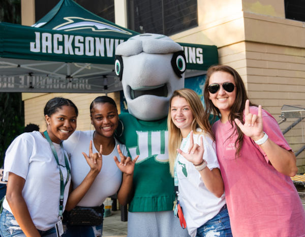 Four students posing with the mascot, Dunkin. 