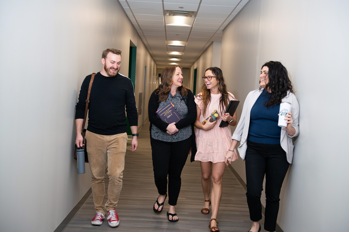 Four students smiling while walking down a hallway in a Jacksonville University building.