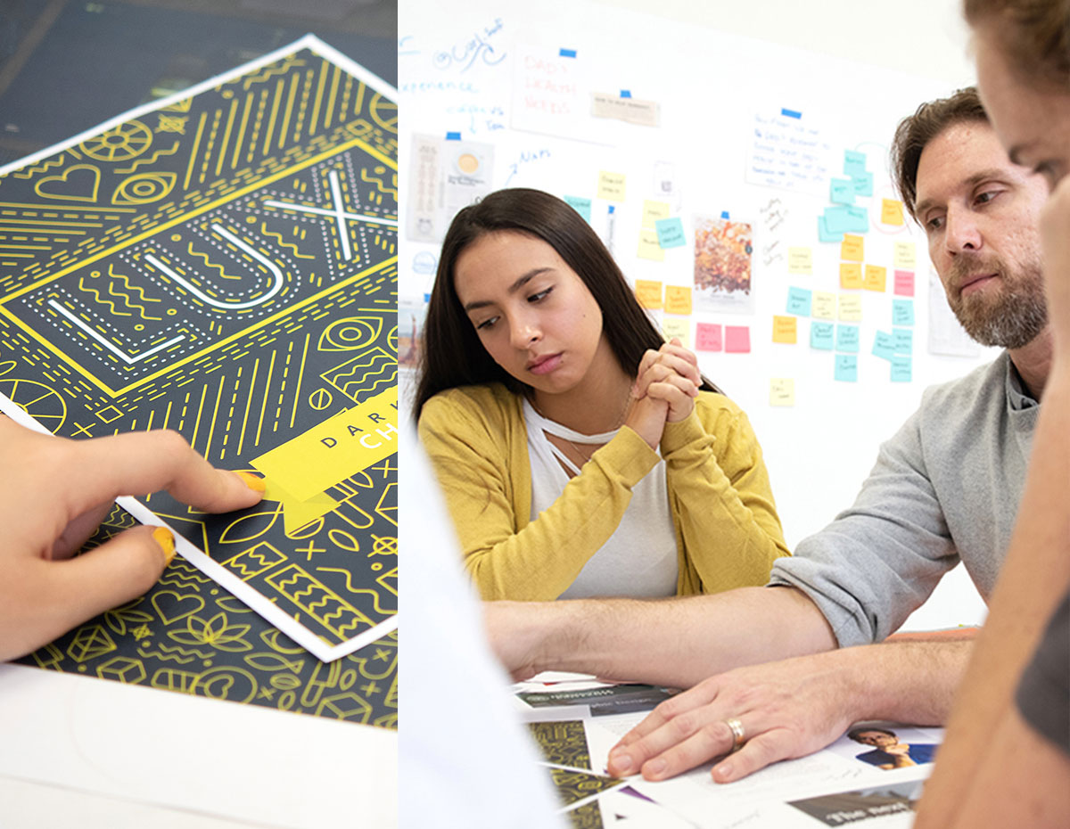 Students sitting at a table reviewing a poster design with instruction and guidance by a design professor.