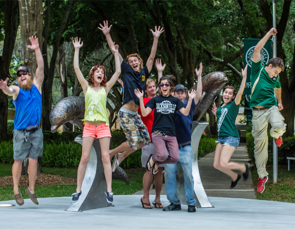 Students jumping in excitement after installing an iconic metal dolphin sculpture on campus.