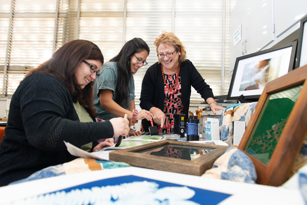 Professor Sheridan in the classroom teaching Alternative Processes photography students how to coat Cyanotype for Sun Prints.