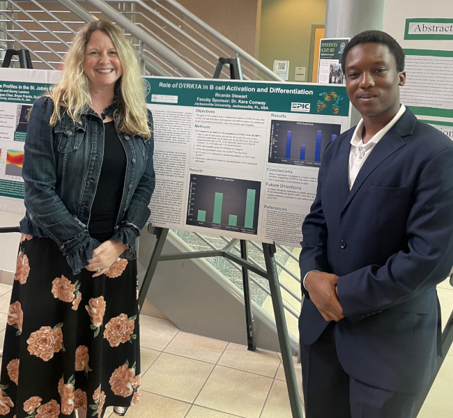 A professor and student posing in front of posters in the Davis College of Business & Technology foyer.