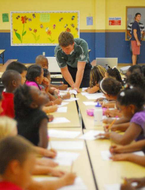 A classroom of young students and a teacher standing up in front of the class.
