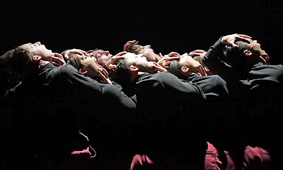 Group of dancers dressed in black on stage with dramatic lighting