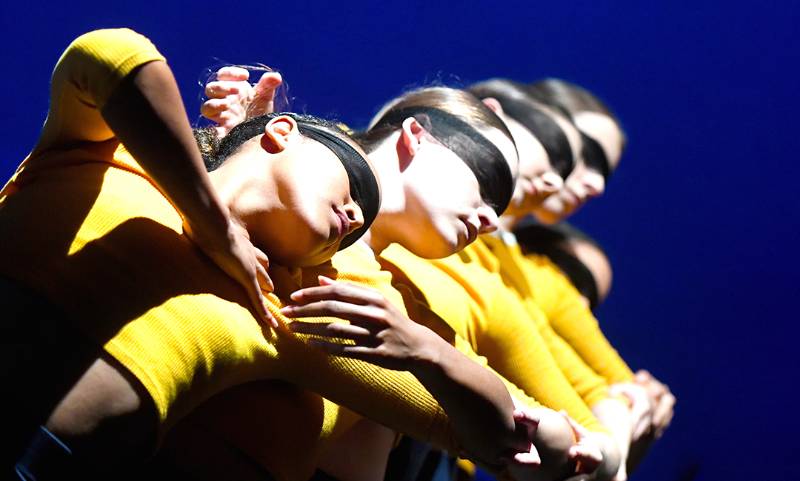 Group of four female dancers in a dramatic pose wearing a black cloth mask