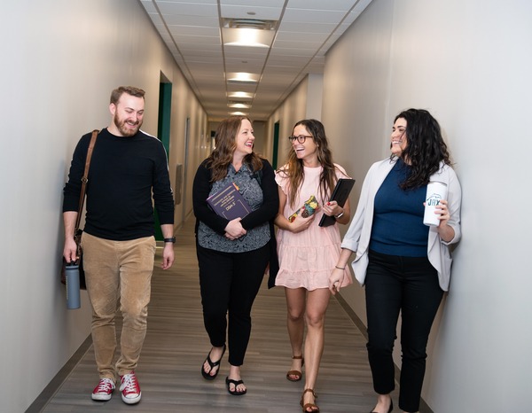 Four students laughing while walking down a corridor in the Davis College of Business building.