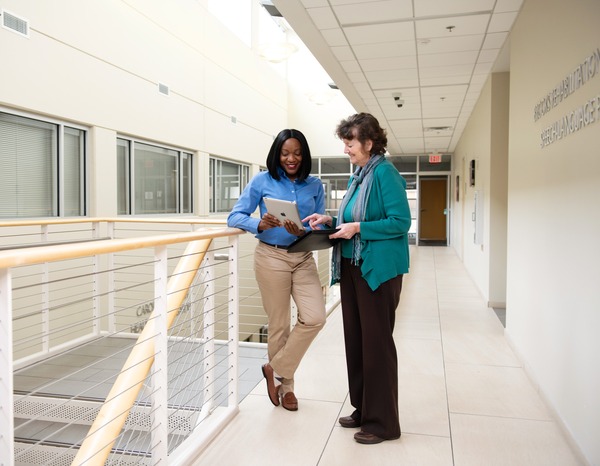 Two female healthcare professional conferring about information on a computer tablet.