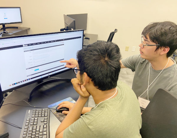 Two students pointing to a laptop in a classroom setting.