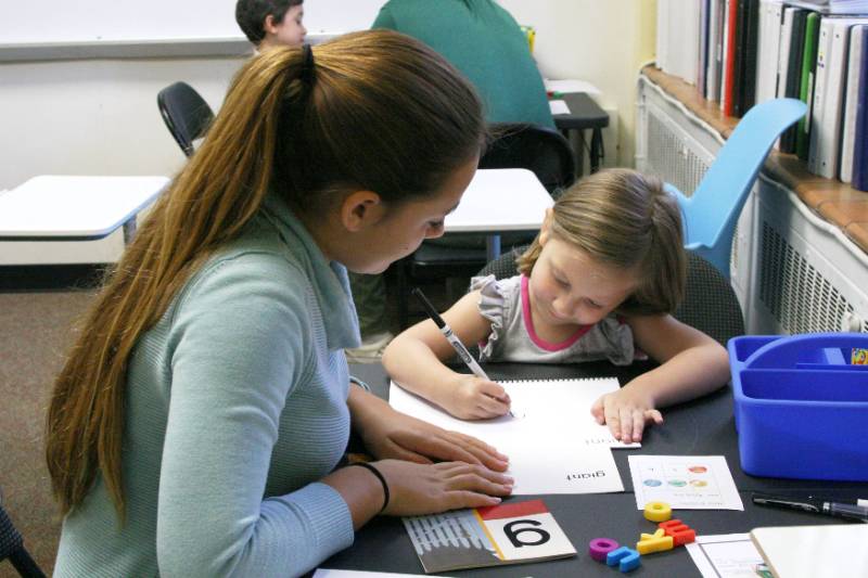 Student teacher helps child learning letters.