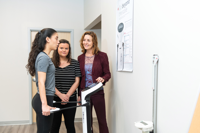 Two students try exercise science equipment while a professor gives instruction