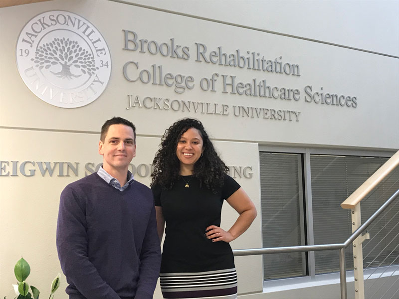 Dr. David Hooper and Dr. Catherine Saenz post on the stairs in the main building of the Brooks Rehabilitation College of Healthcare Sciences.