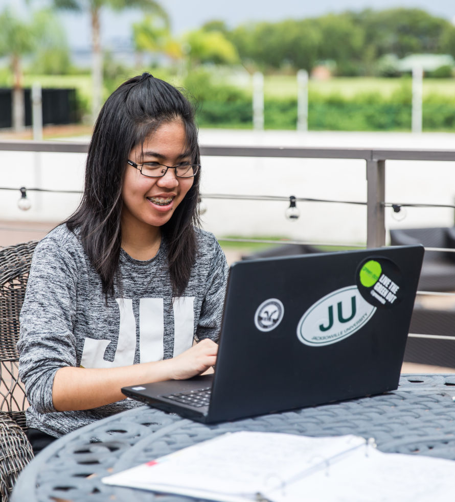 A student seating at an outdoor table with her laptop.