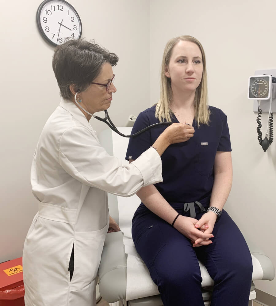 A female medical doctor using a stethoscope to exam a female patient's chest in a medical office table.
