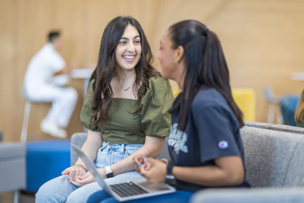 Two female students sitting at JU Kinne Center, one student holds a laptop on her lap. 