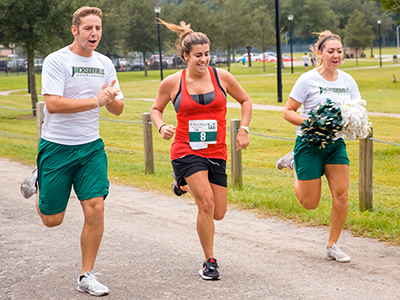 A runner with cheerleaders at the River House Run