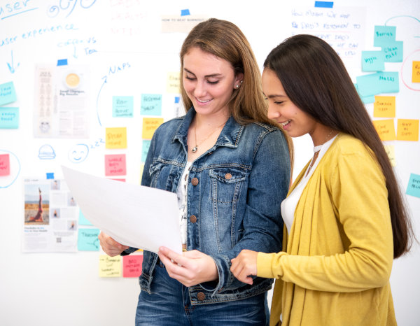 Two women in front of a white board brainstorming ideas. 