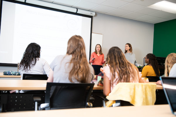 A professor leading a class discussion in a classroom full of students sitting at desks.