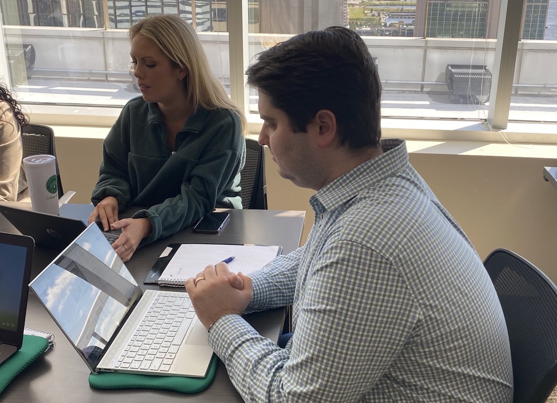 A male and female student sitting a table using their laptops together, seemingly to work on a group project.