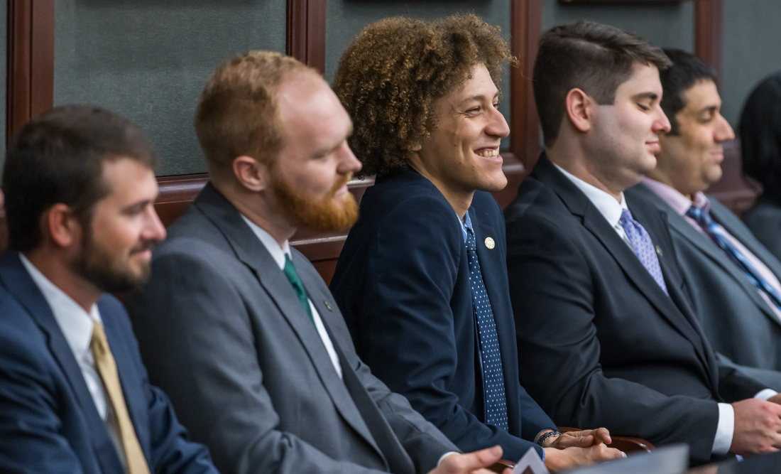 A group of male students sitting in a courtroom jury box, smiling. 