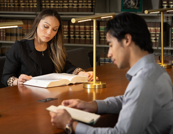 Two of law students seating at a library desk with open books on their table. 