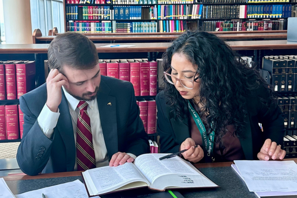 Two students reading a law textbook together in a legal library.