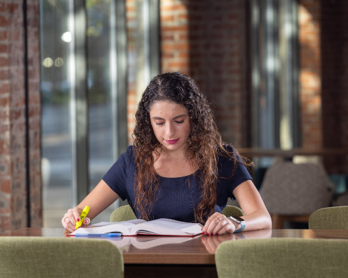 A female student sitting a table using her laptop, seemingly to work on a group project.
