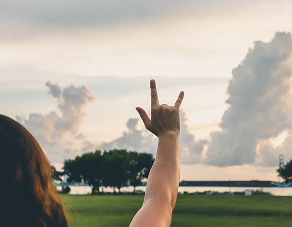 A hand holding up the 'Phins Up' symbol with fingers extended to create a J and a U against a bright sky.