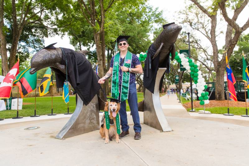 A military veteran standing at the dolphin statue after graduation.