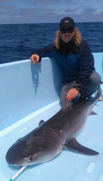 a man with blonde curly hair smiling with a shark on a boat