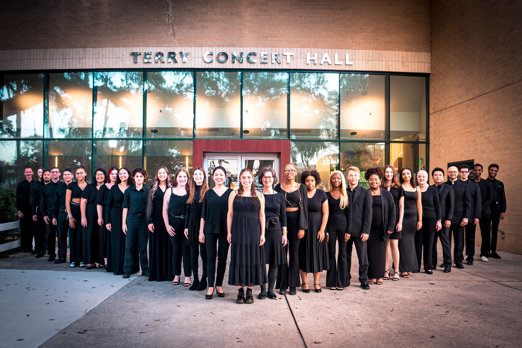 Group photo of a choir standing in a v-formation in front of Terry Concert Hall's main entrance.