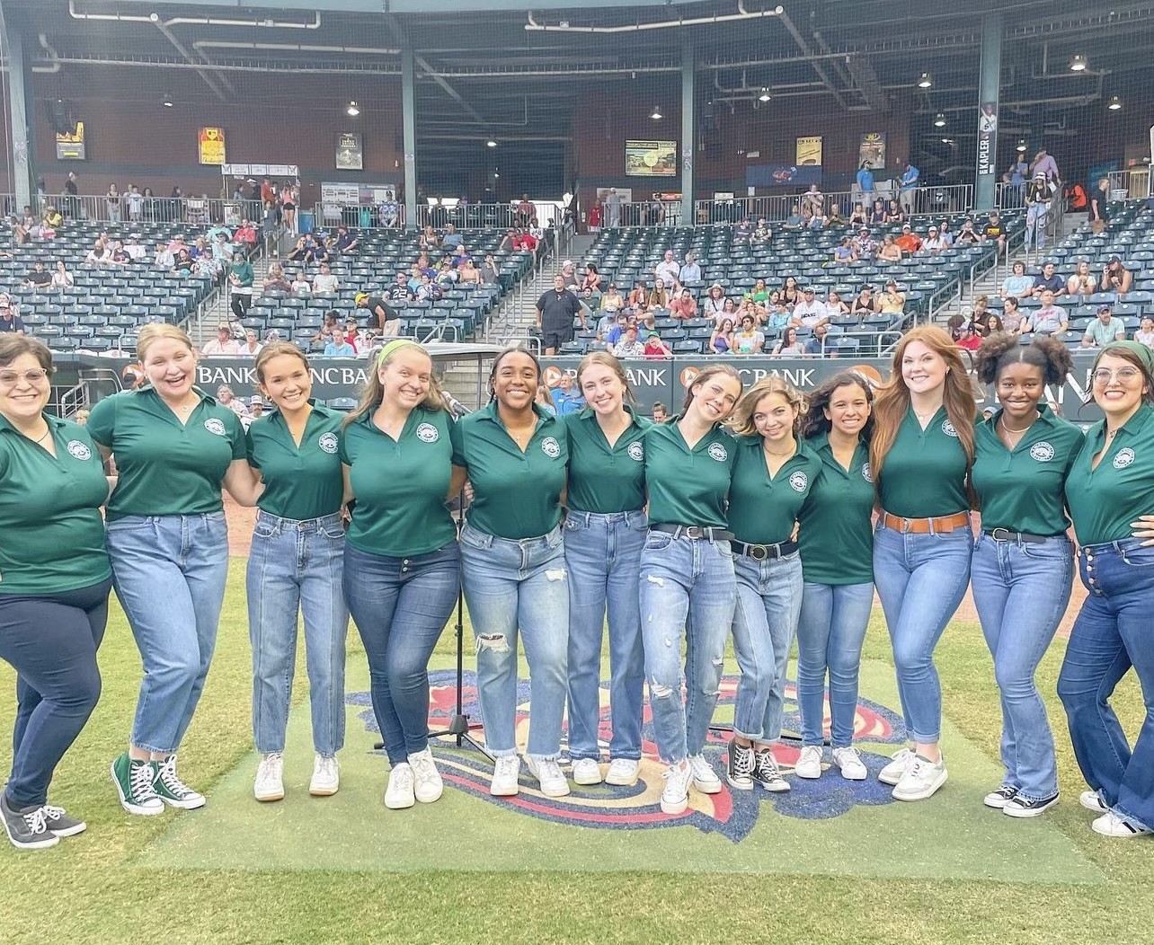 A female vocal ensemble in front of a stadium, arm in arm