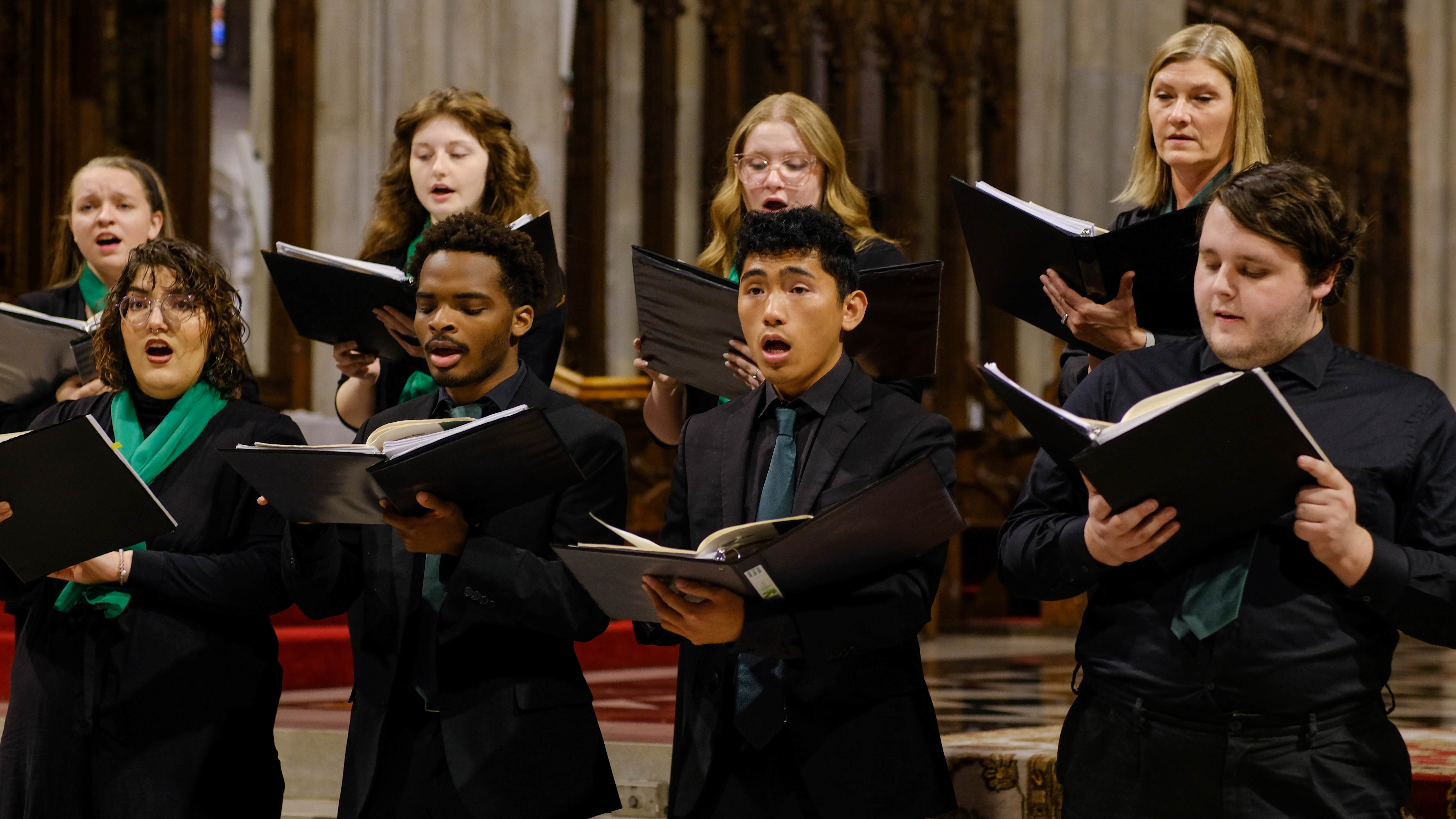 The Jacksonville University singers are pictured dressed in black professional attire and green scarves and ties, singing emotively at the St. Patrick's Cathedral