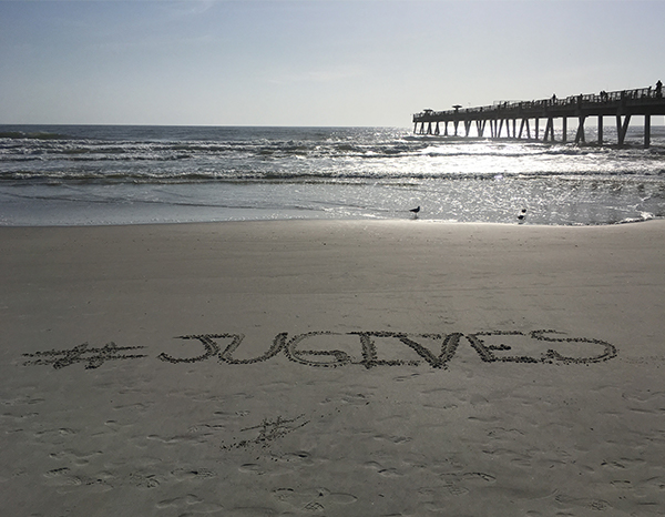 Hashtag JU Gives written in the sand.