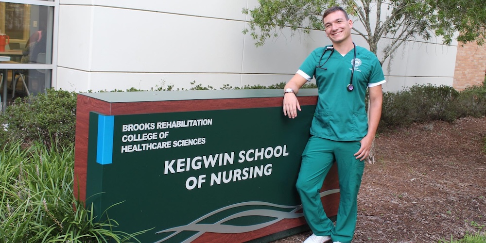 Seth Roster standing beside Keigwin School of Nursing sign