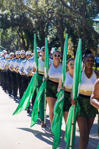 The JU colorguard team walking down the street holding green flags.