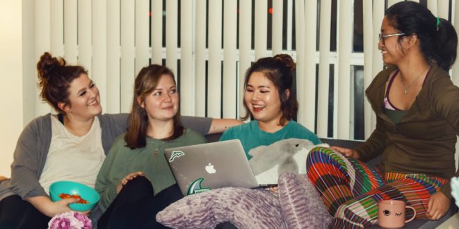 Four female students sit on a couch together smiling and laughing
