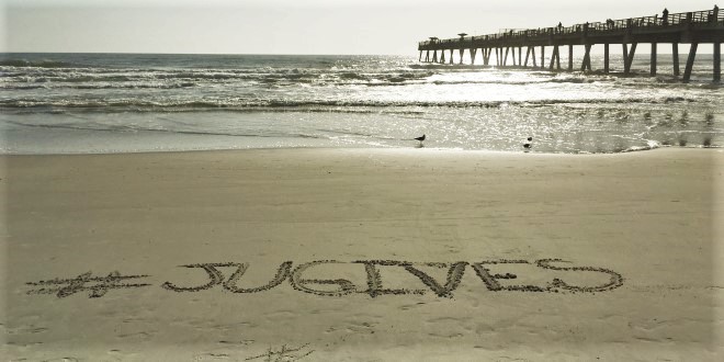 Photo of the beach with #JUGives written in the sand.