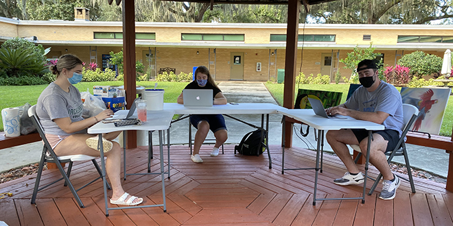 Three students sitting at tables with laptop computers.