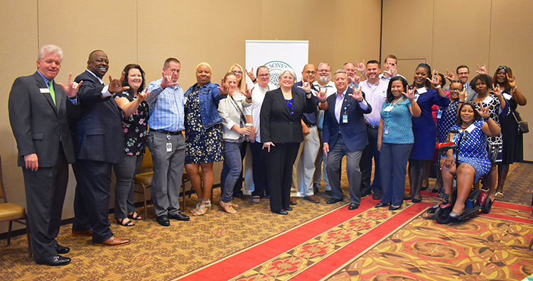 A group of Florida Blue employees and JU President Tim Cost throwing up the JU "Phins UP" hand sign