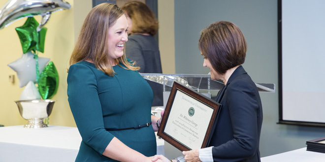Whitney George embracing Dr. Sherri Jackson while accepting an award plaque for the 2019 Faculty Excellence Award