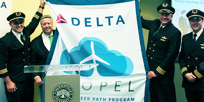 President Cost standing with members of the Delta Propel team, holding a large Delta Propel banner.