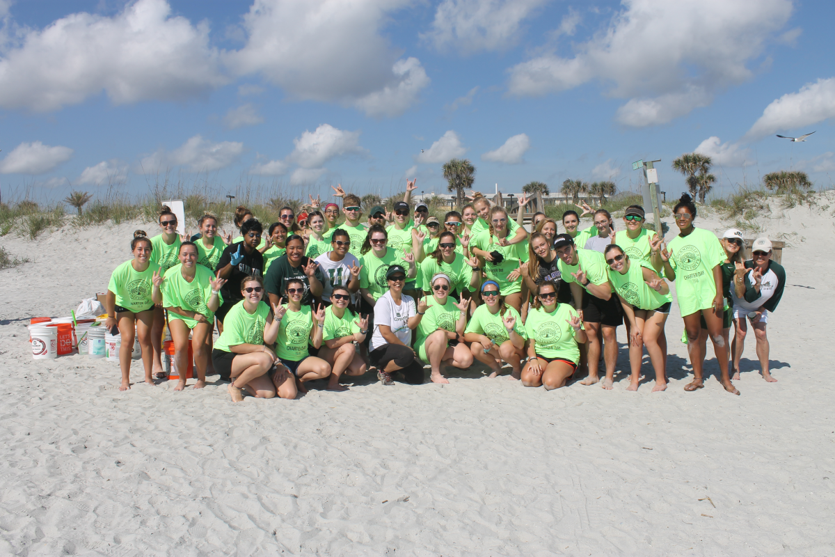 Group of JU students posing in a large group at the beach during Charter Day 2019