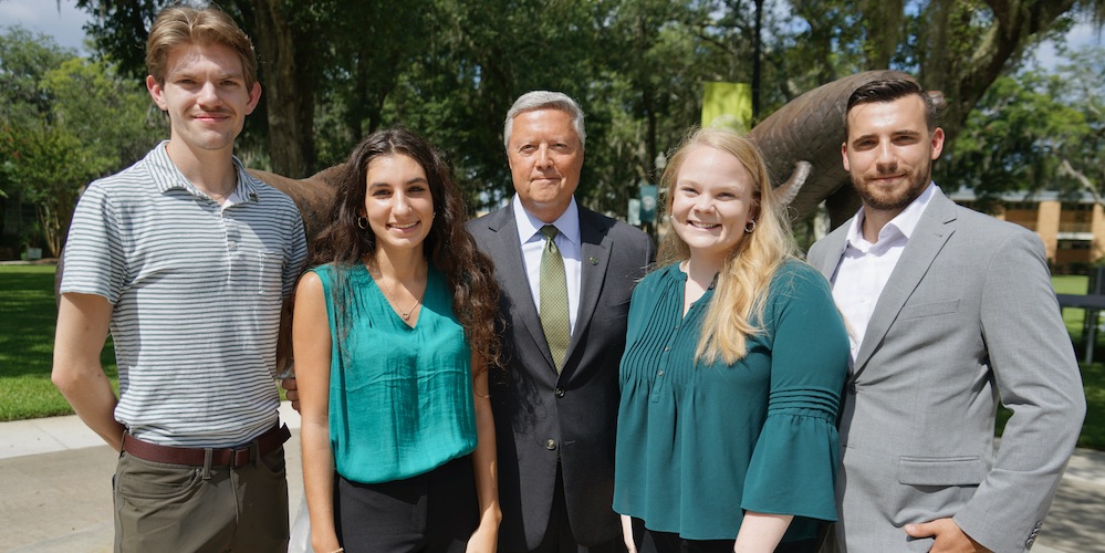 four JU alumni pose with President Tim Cost